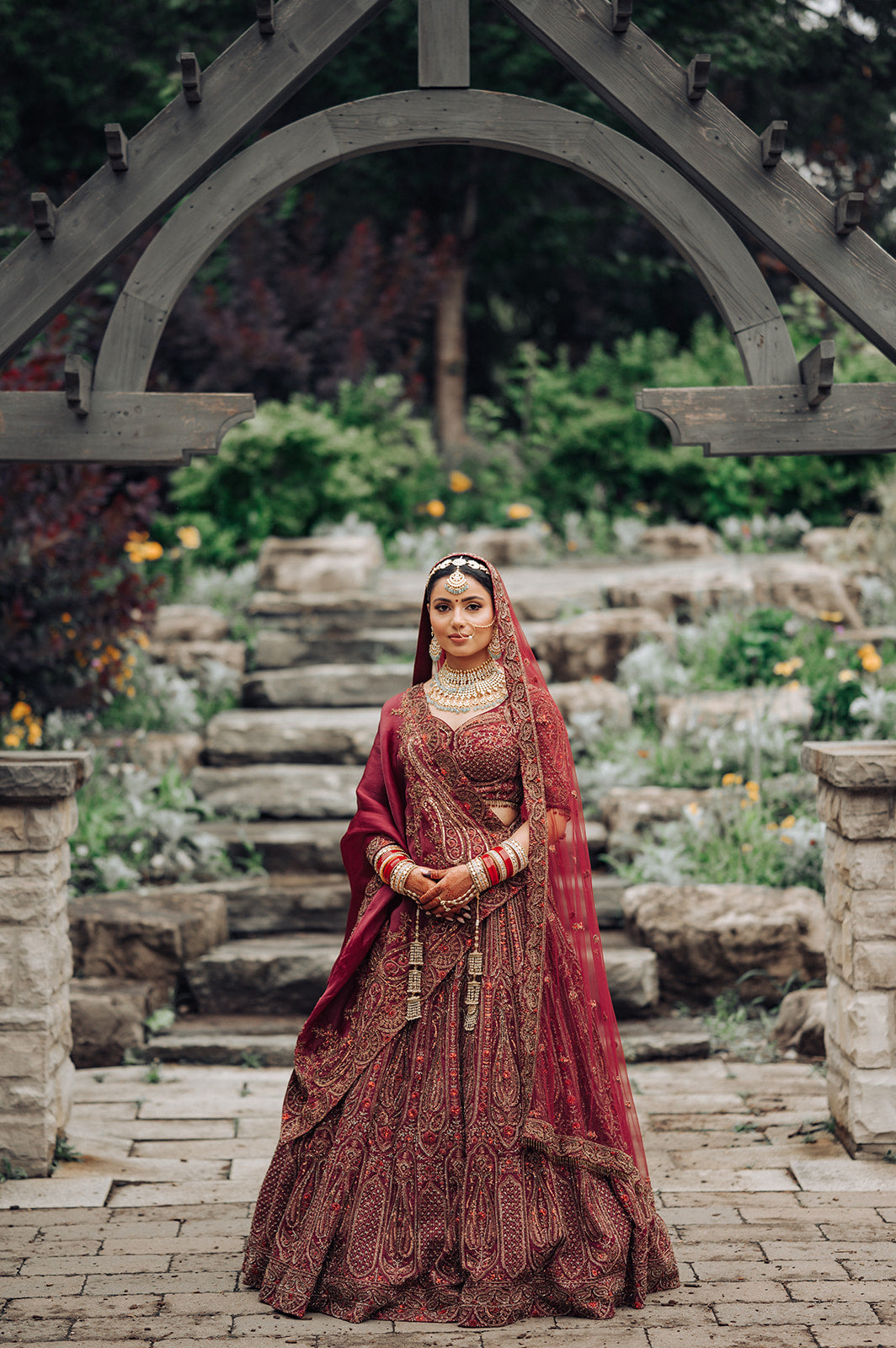 Asopalav bride in a maroon bridal lehenga in a garden setting